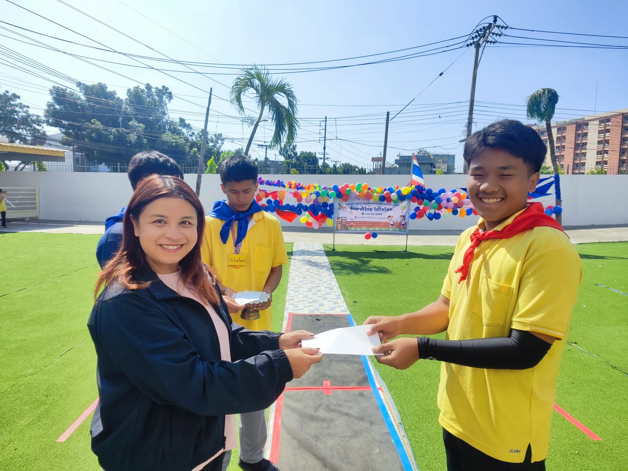 A Kong Lah School student receiving an award from a teacher outdoors.