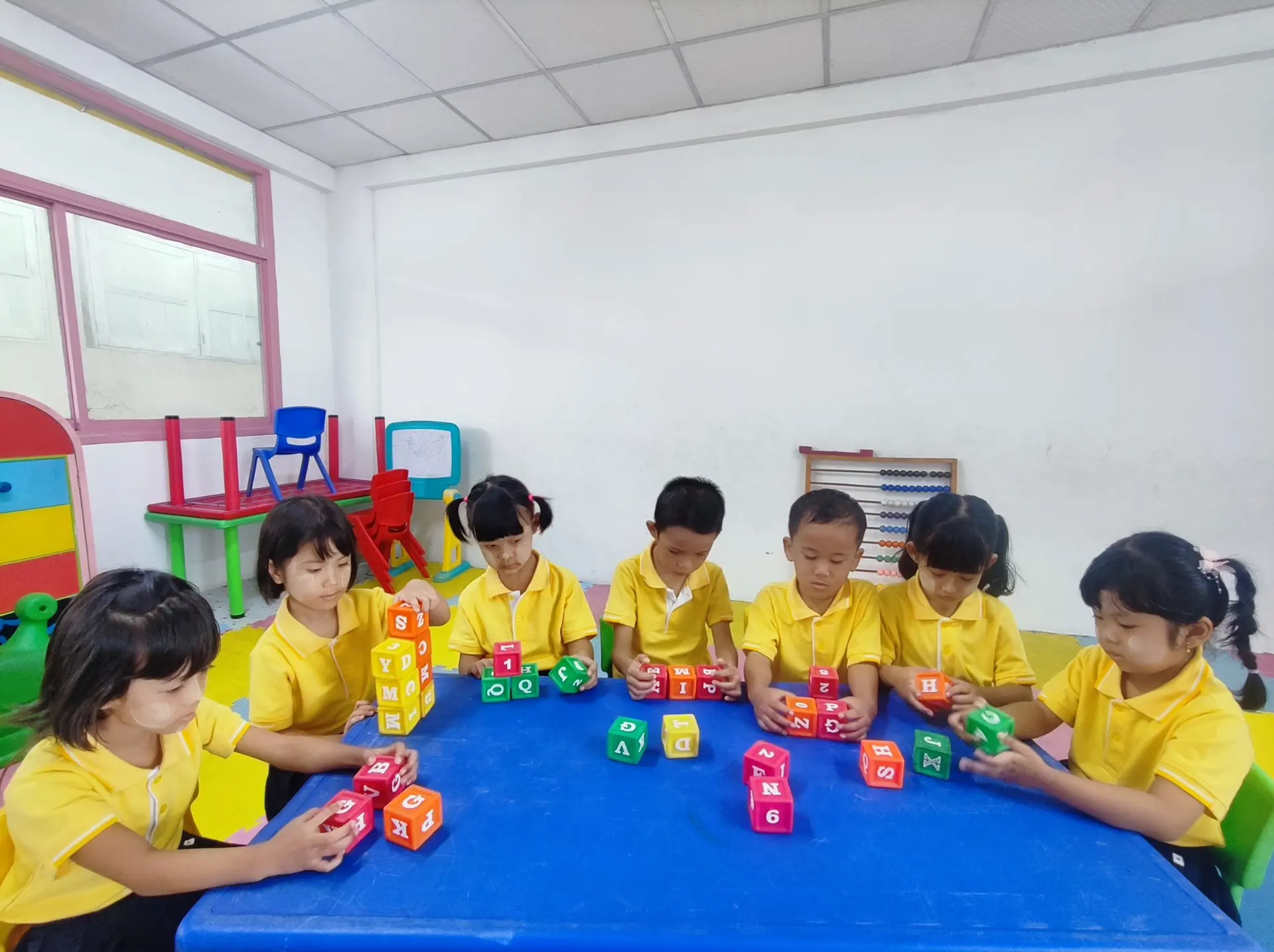 Young Kong Lah School students learning with colorful letter and number blocks.