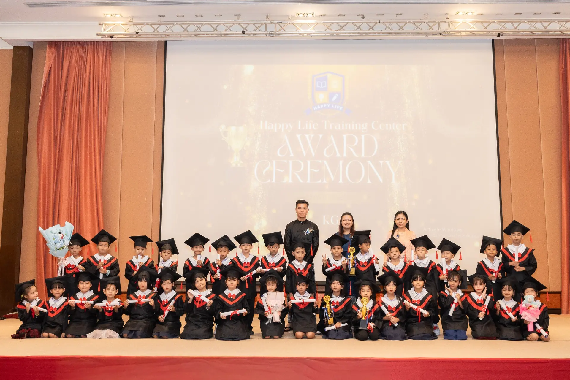 Young Kong Lah School graduates posing with their teachers, diplomas, and trophies.
